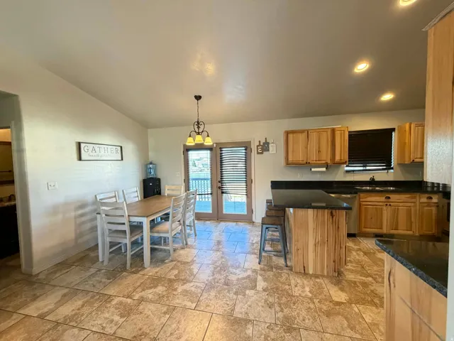 Kitchen with a breakfast bar area, light stone finish floors, lofted ceiling, wood finish cabinets, and hanging light fixtures