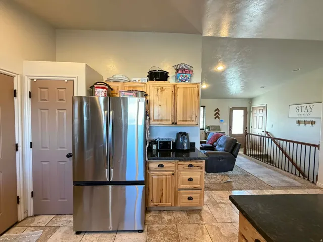 Kitchen with freestanding refrigerator, vaulted ceiling, light wood finish cabinets, open floor plan, and dark stone counters