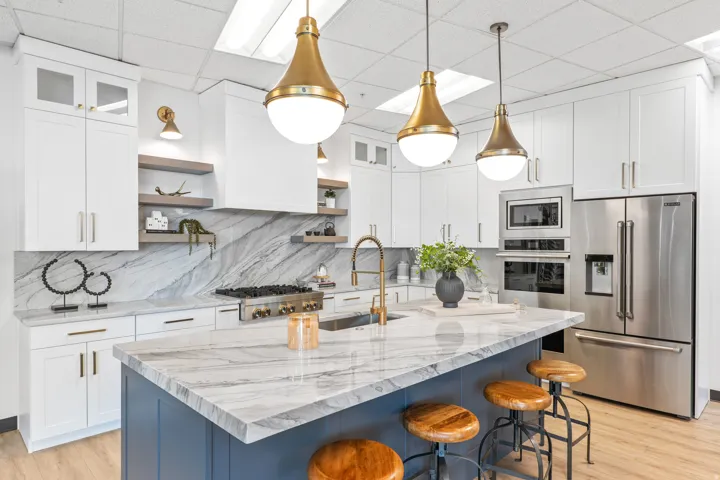 Kitchen with stainless steel appliances, a kitchen island with sink, glass insert cabinets, light stone counters, and light wood finished floors