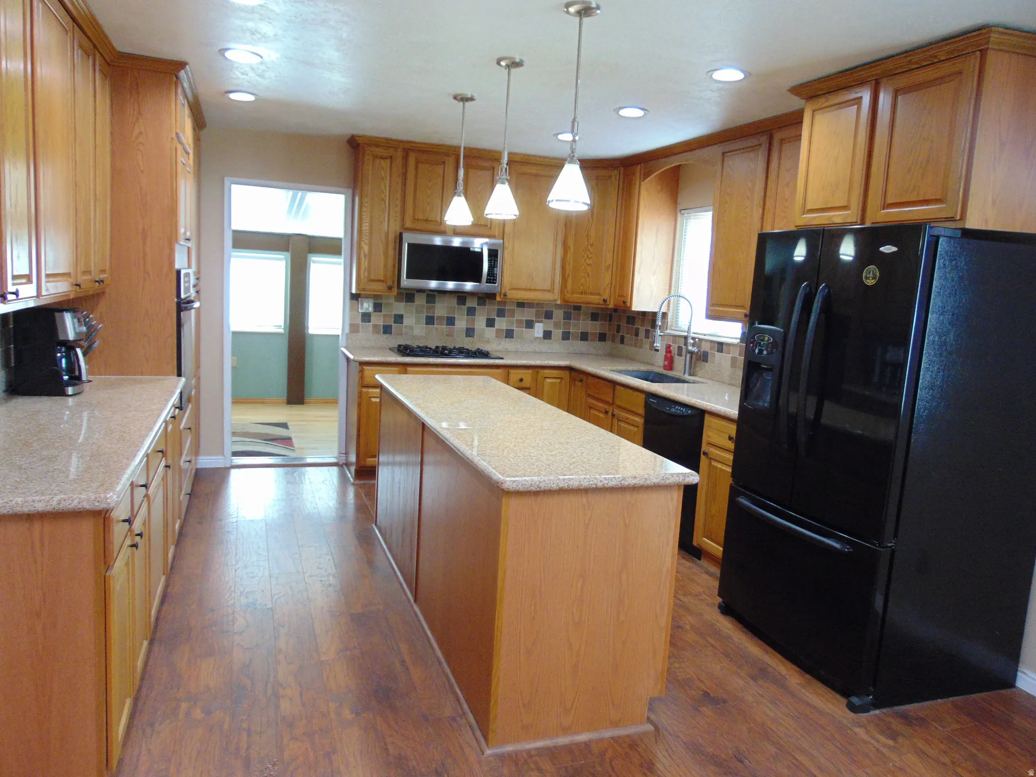 Kitchen with black appliances, dark wood-style floors, hanging light fixtures, a center island, and light stone countertops