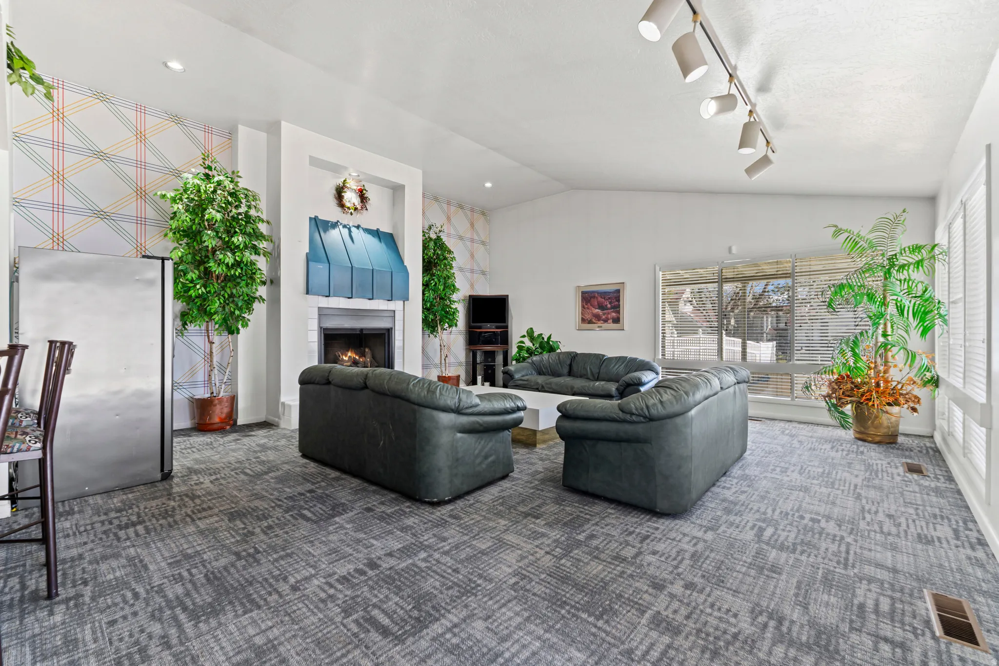 Living area with carpet, a lit fireplace, vaulted ceiling, and rail lighting