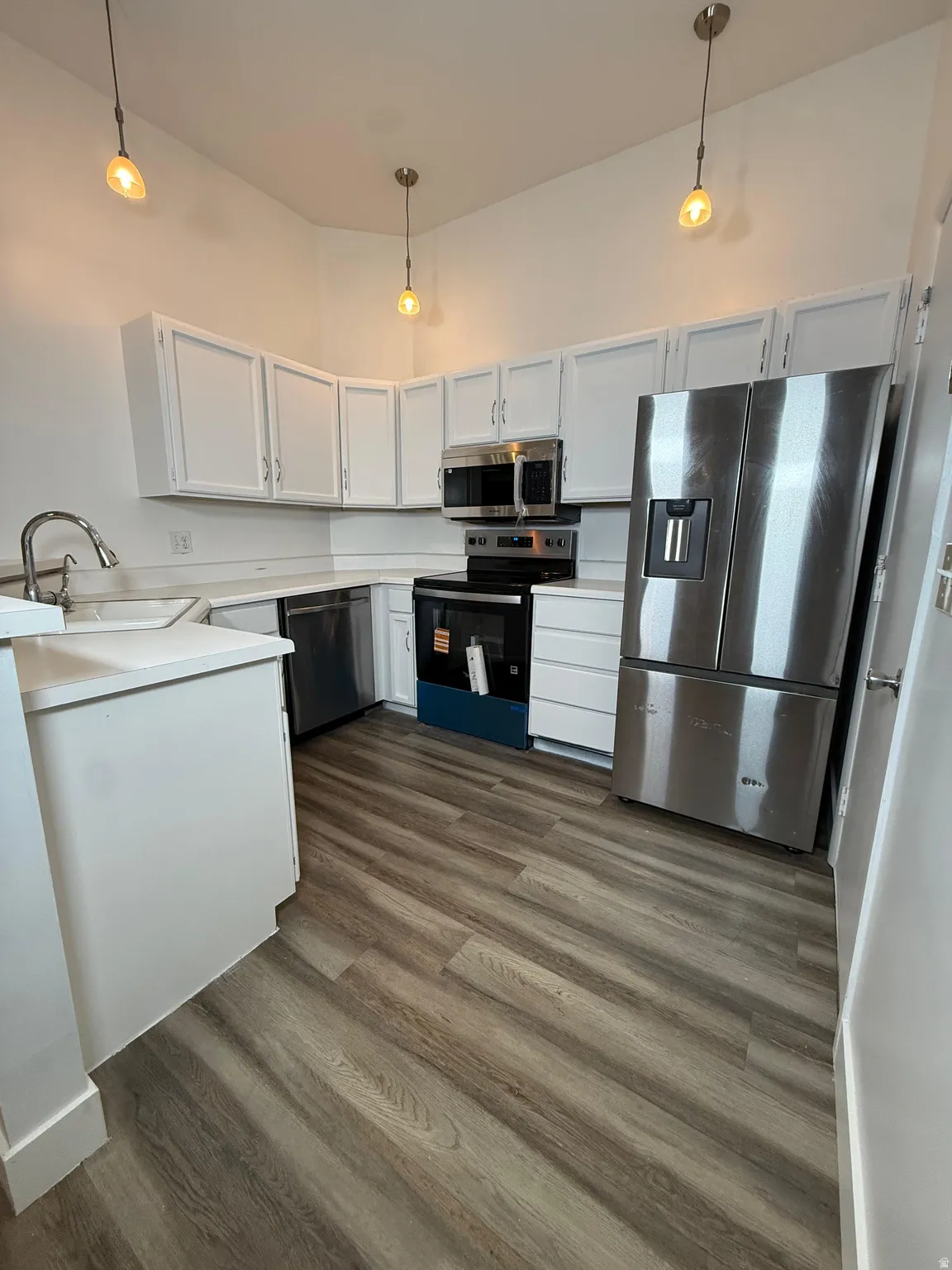 Kitchen featuring light countertops, stainless steel appliances, white cabinetry, hanging light fixtures, and a high ceiling