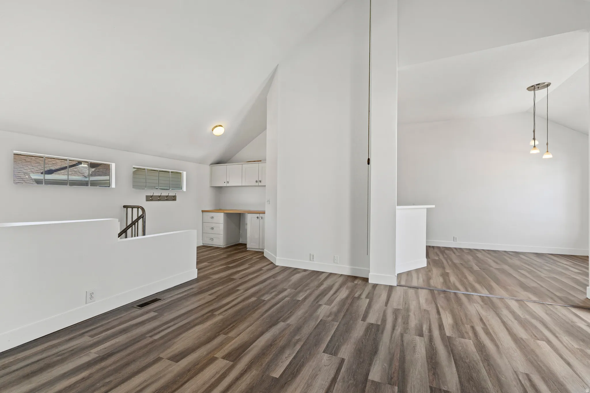 Unfurnished living room with built in desk, vaulted ceiling, and dark wood-type flooring