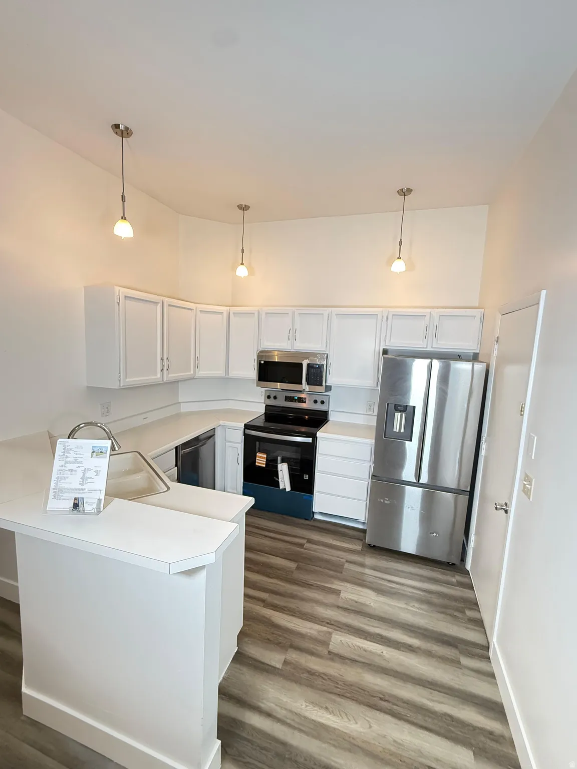 Kitchen featuring stainless steel appliances, light countertops, a peninsula, white cabinetry, and dark wood finished floors