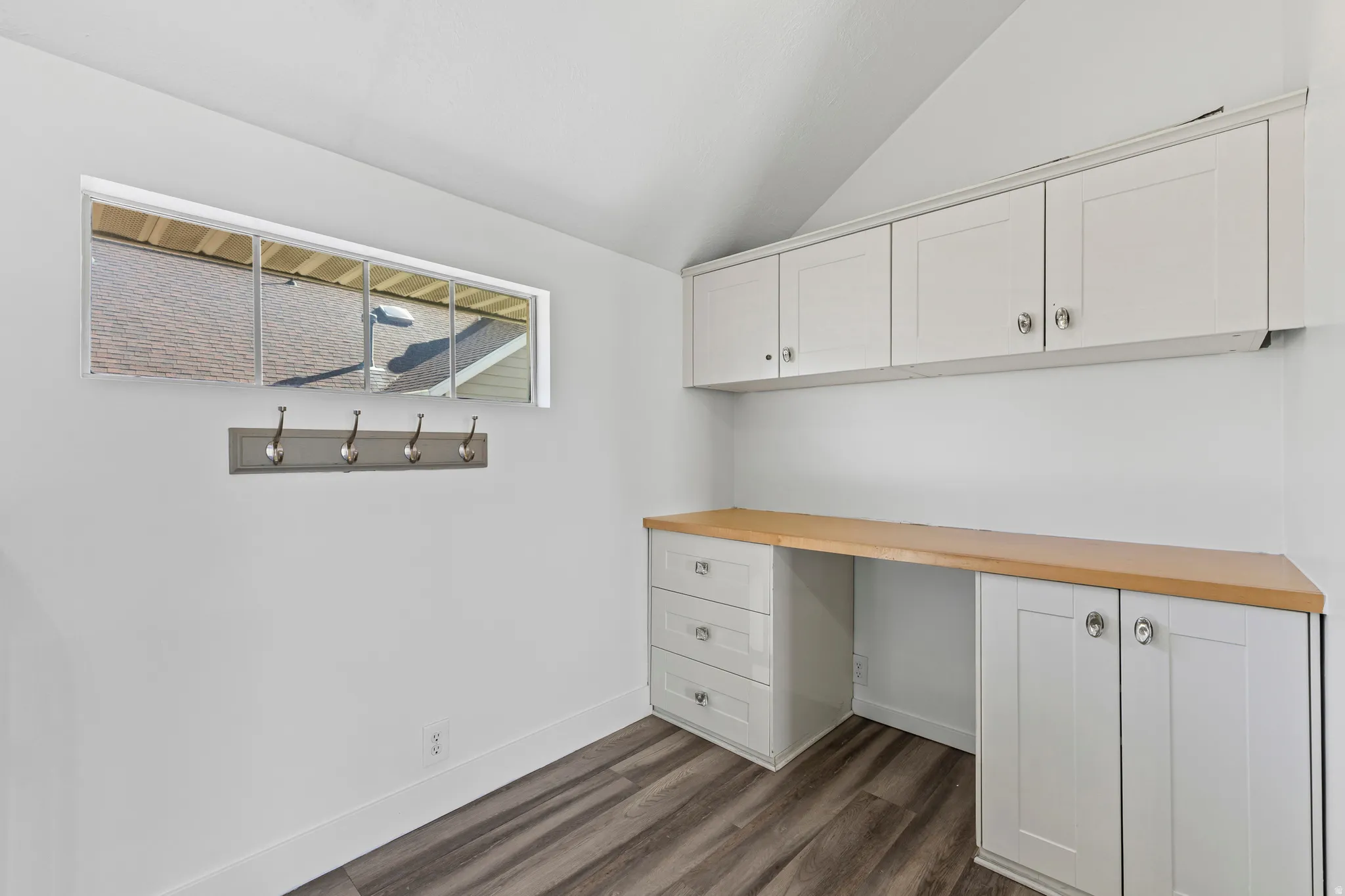 Unfurnished office featuring built in desk, dark wood-type flooring, and lofted ceiling