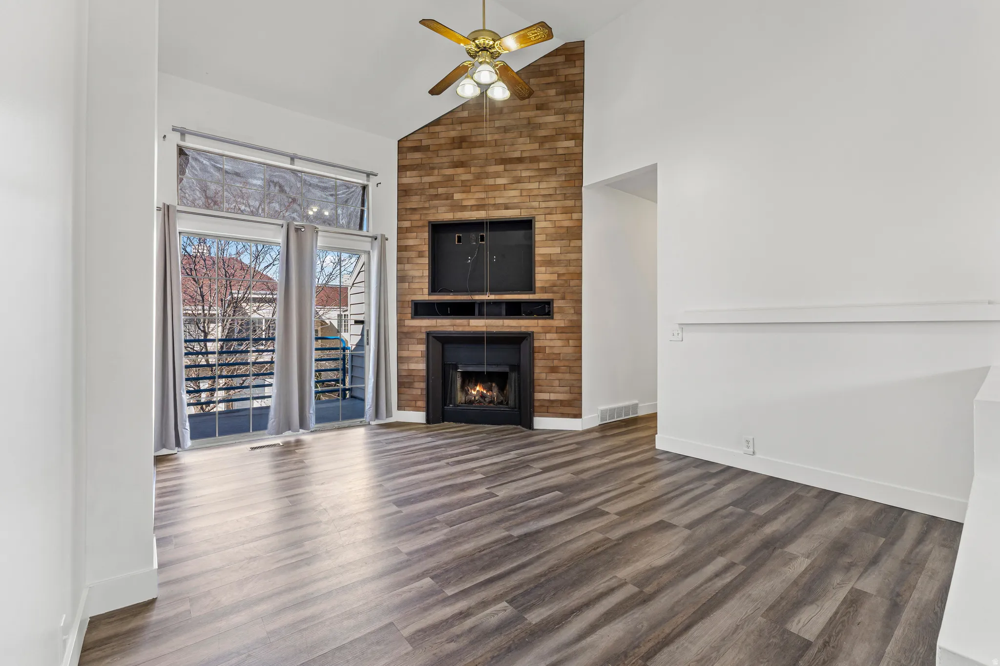 Unfurnished living room featuring vaulted ceiling, ceiling fan, dark wood-type flooring, and a fireplace