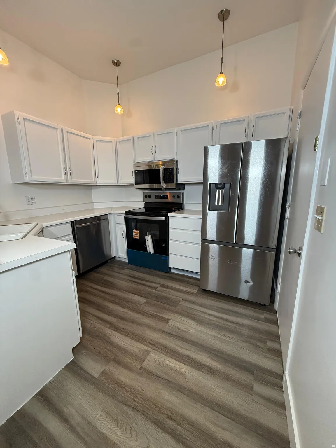 Kitchen featuring white cabinets, light countertops, stainless steel appliances, and hanging light fixtures