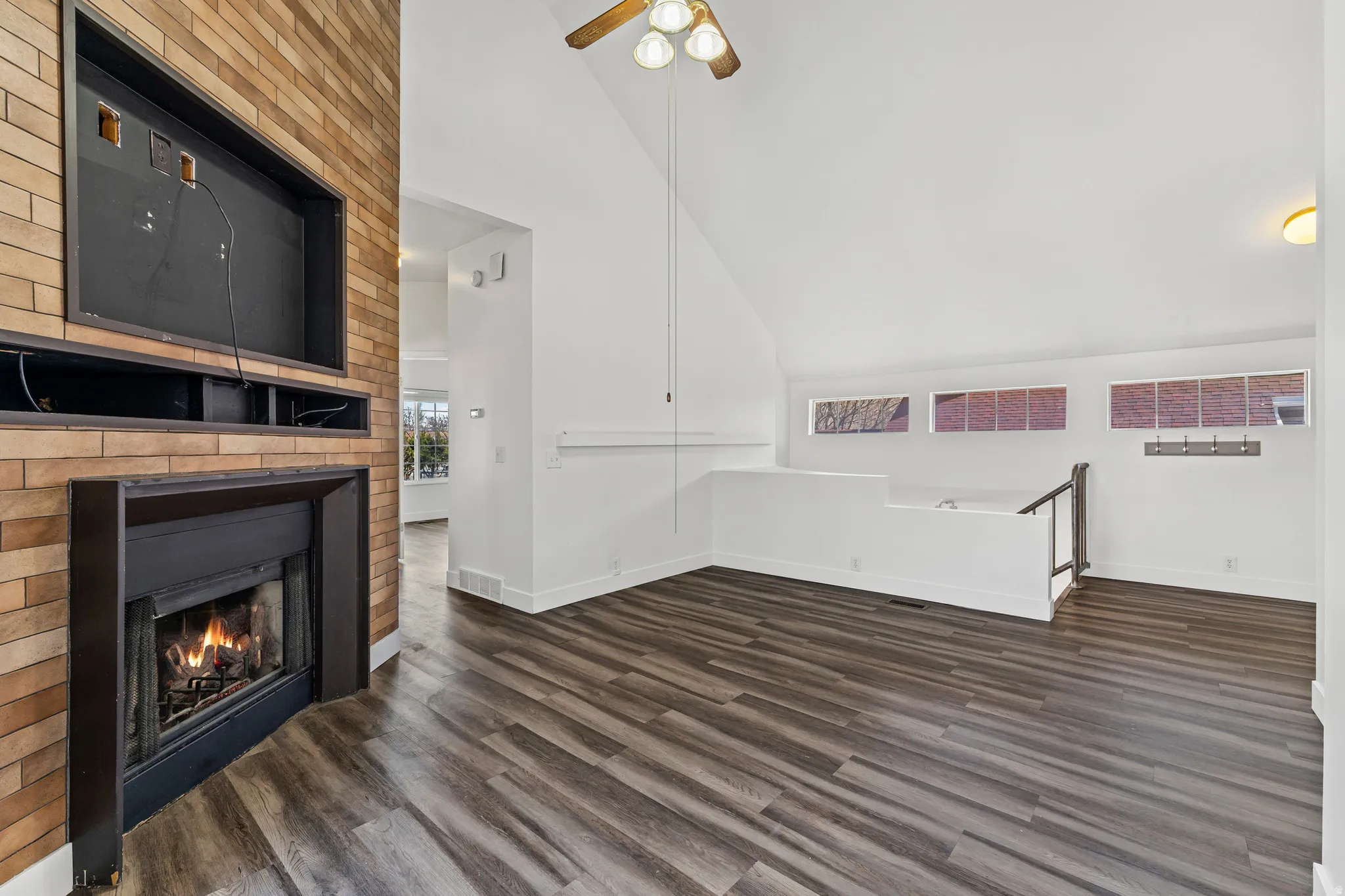 Unfurnished living room featuring lofted ceiling, ceiling fan, a fireplace, and dark wood finished floors
