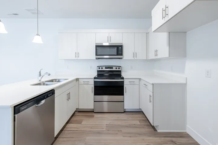 U-shaped kitchen featuring white cabinetry, light-colored countertops, wood-finish flooring, and stainless steel appliances