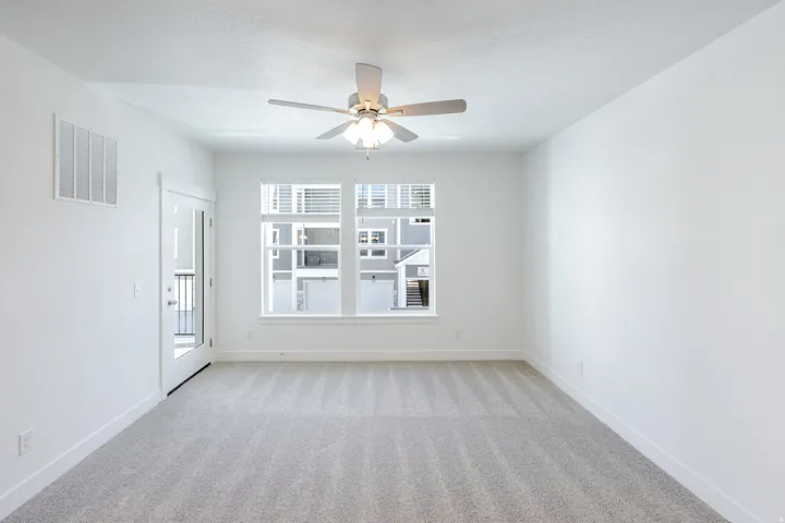 Neutral-toned carpeting, white walls, large multi-pane window, ceiling fan with integrated lighting, and a glass-paneled door