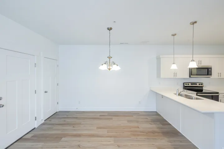 Open-concept kitchen and dining area featuring white cabinetry with stainless steel appliances, white quartz countertops, pendant lighting, and wide-plank wood-finish flooring throughout the space