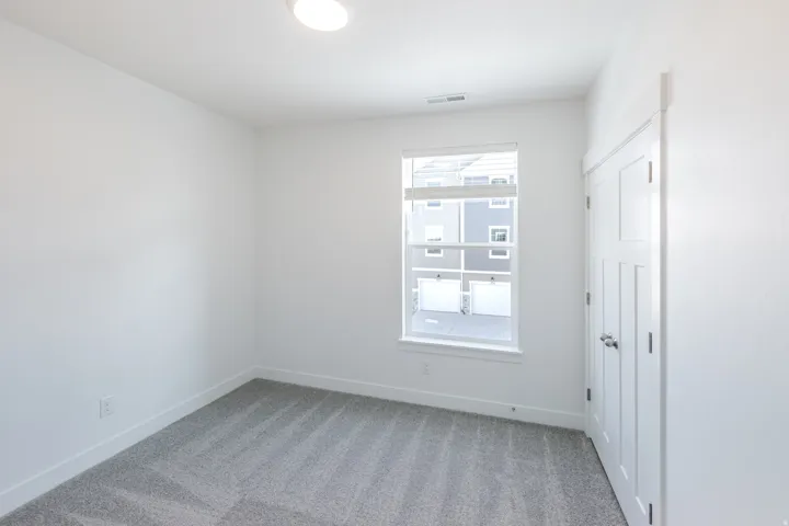 Neutral white walls, plush gray carpeting, recessed ceiling lighting, a multi-pane window, and a paneled interior door