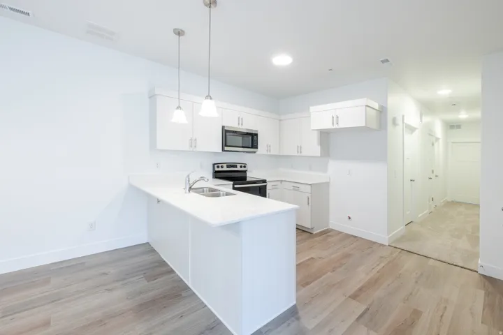 Modern kitchen featuring white cabinetry, stainless steel appliances, a breakfast bar, light countertops, and wood-finish flooring