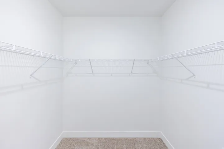 Integrated wire shelving system with white finish, L-shaped configuration, light-toned carpeting, and crisp white walls