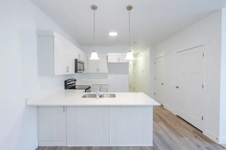 Kitchen featuring white cabinetry, light countertops, wood-finish flooring, stainless steel appliances, and pendant lighting