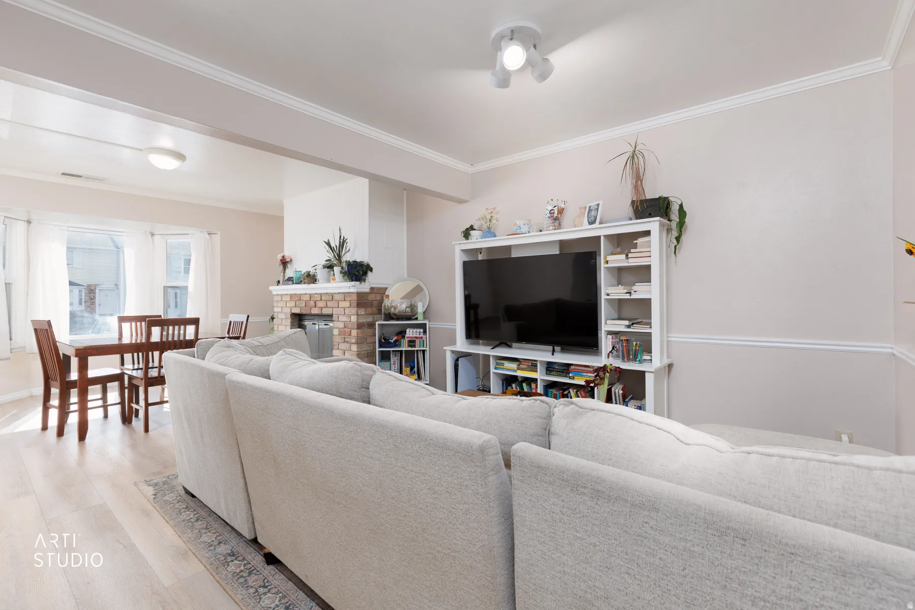 Living area featuring light wood-type flooring, crown molding, and a fireplace
