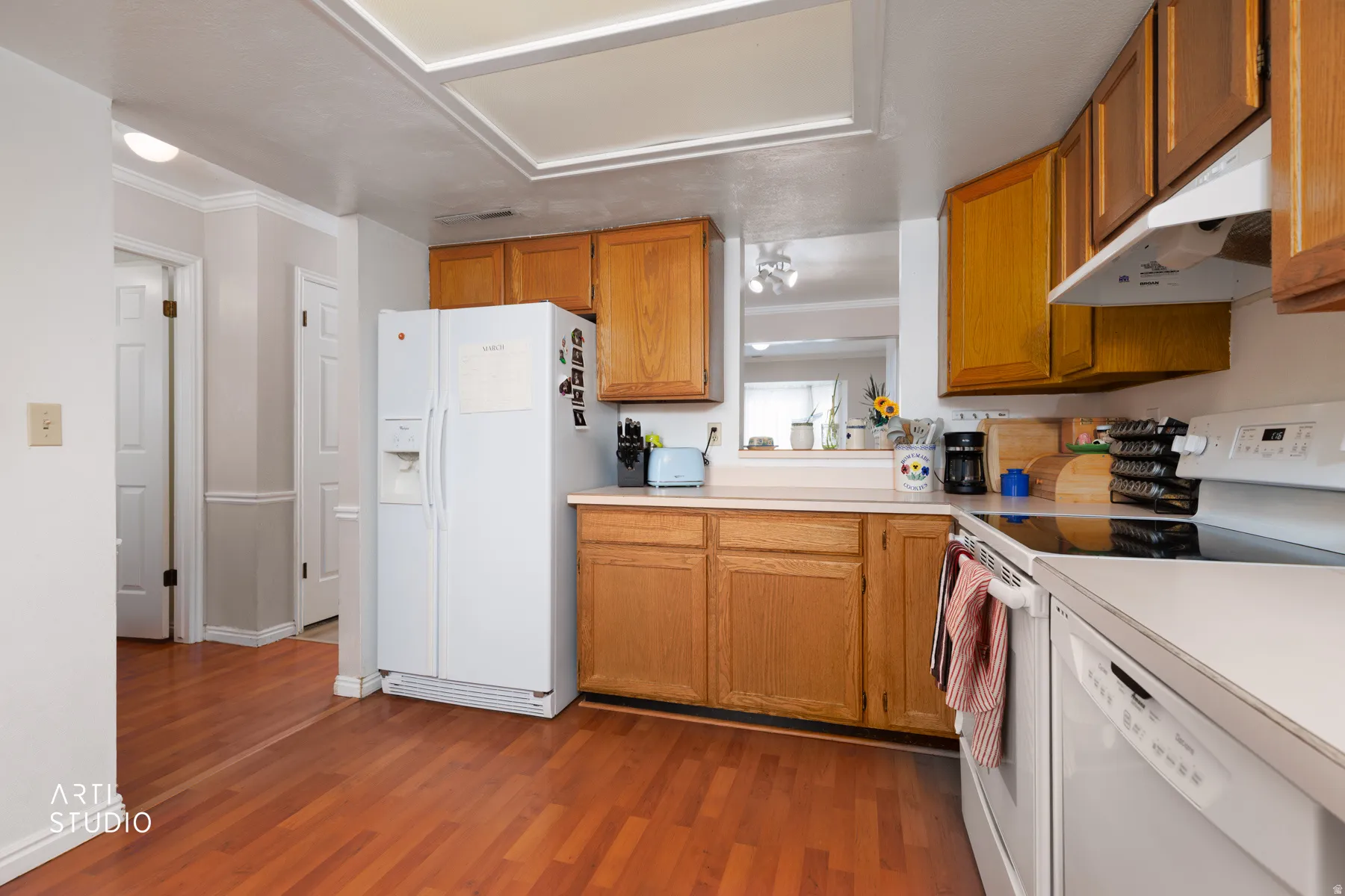 Kitchen with white appliances, light countertops, light wood-type flooring, wood finish cabinets, and ornamental molding