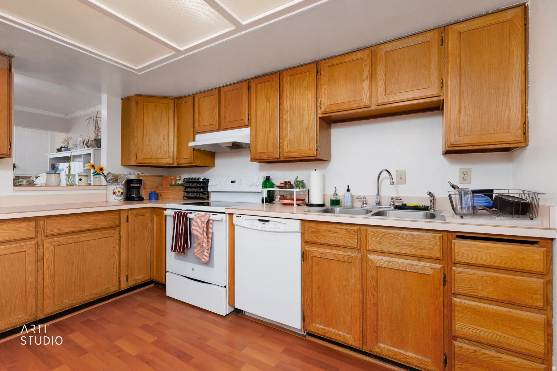 Kitchen with light countertops, white appliances, light wood-type flooring, wood finish cabinets, and crown molding