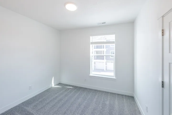 Recessed ceiling lighting, white walls, light gray patterned carpet, white window frame, and a white door with panel detailing