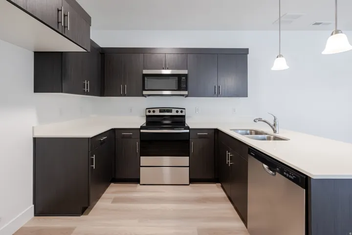 U-shaped kitchen featuring dark wood-finish cabinetry, light-toned countertops, stainless steel appliances, and wood-finish flooring