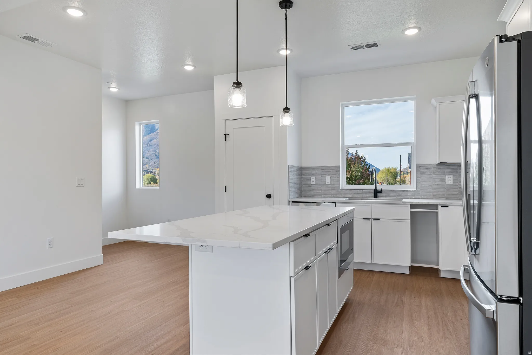 Kitchen featuring white cabinets, stainless steel appliances, light wood-style floors, a kitchen island, and hanging light fixtures