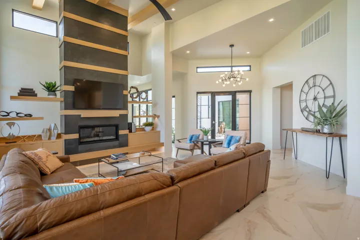 Living room with a fireplace, light marble finish floors, a high ceiling, and a chandelier