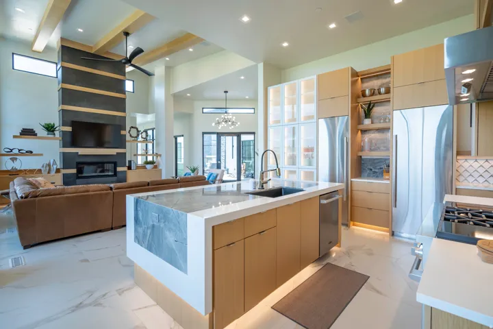 Kitchen featuring modern cabinets, light wood finish cabinetry, a center island with sink, extractor fan, and light stone counters
