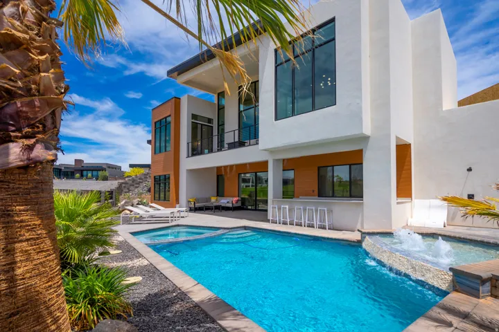 Rear view of house featuring a balcony, stucco siding, a patio area, a pool with connected hot tub, and an outdoor lounge area with bar