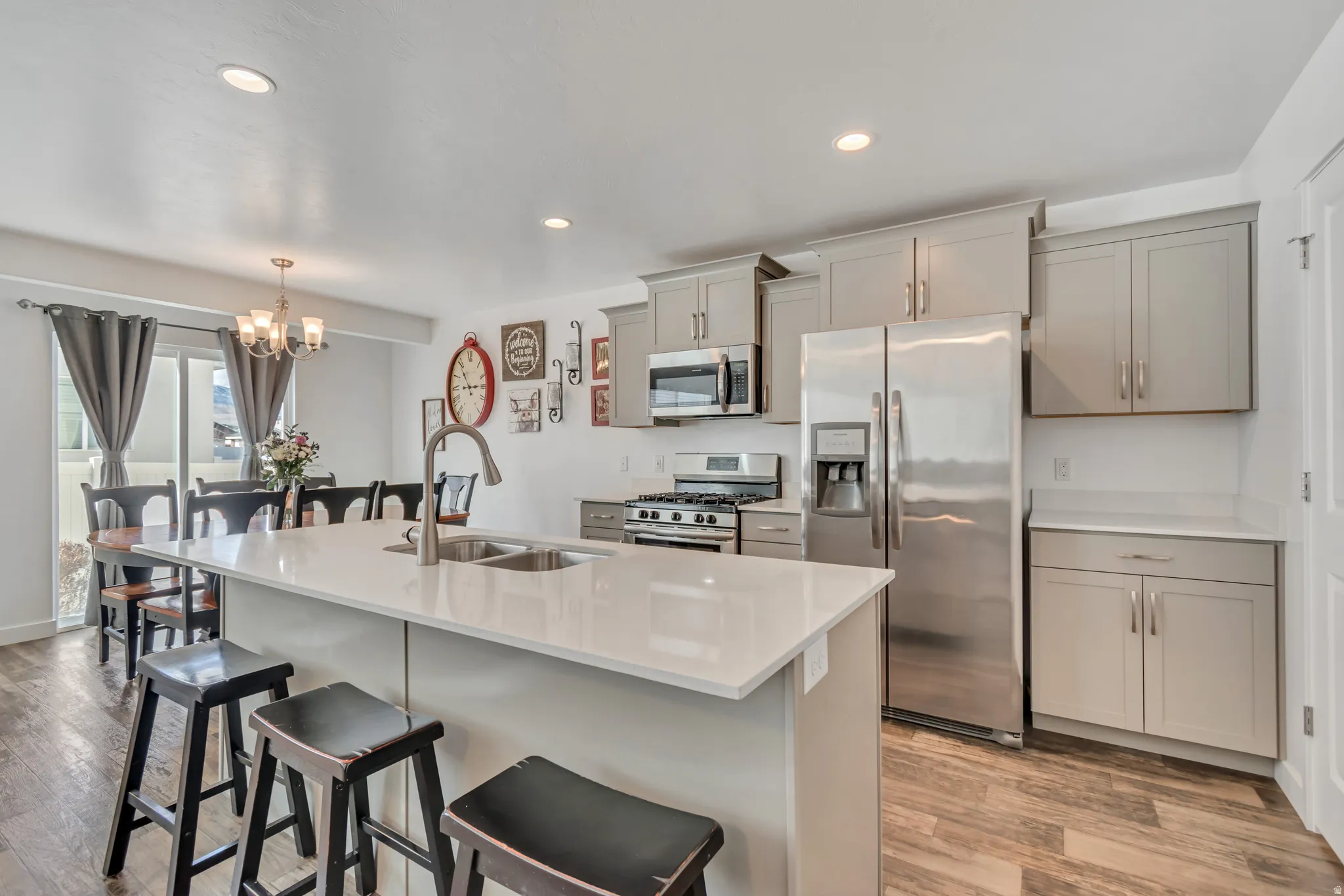 Kitchen with stainless steel appliances, gray cabinetry, a breakfast bar, light wood-style flooring, and a chandelier