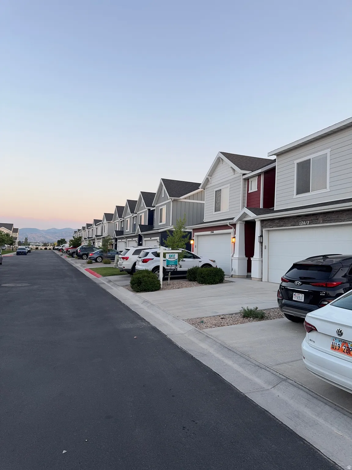 Row of modern townhomes featuring varying facade colors, attached garages, and a paved street