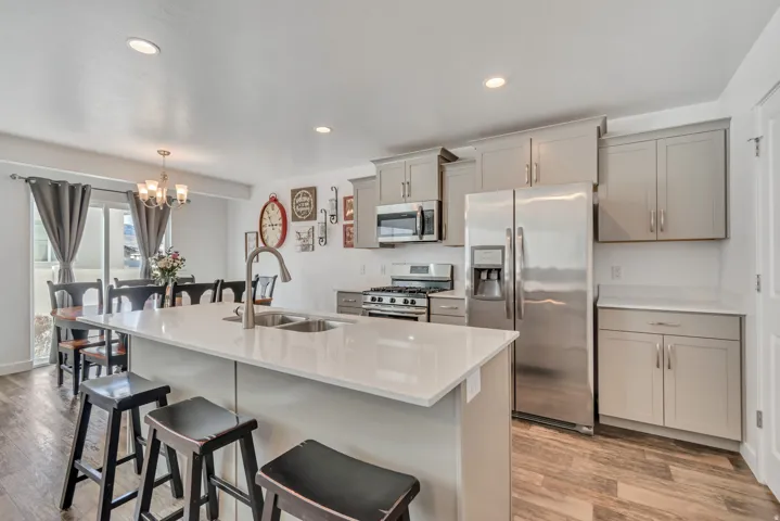 Kitchen with stainless steel appliances, gray cabinetry, a breakfast bar, light wood-style flooring, and a chandelier