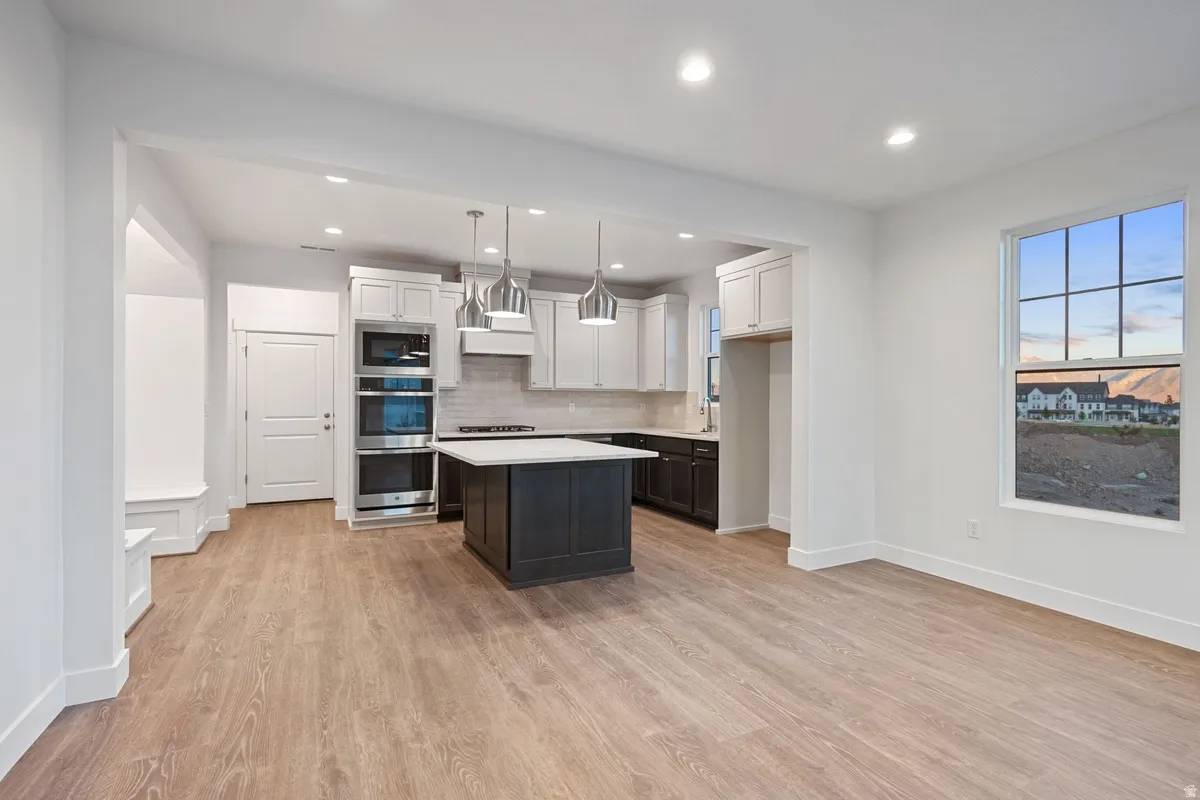 Dual tone kitchen featuring a center island, stainless steel appliances, light wood finished floors, dual tone cabinets, and hanging light fixtures