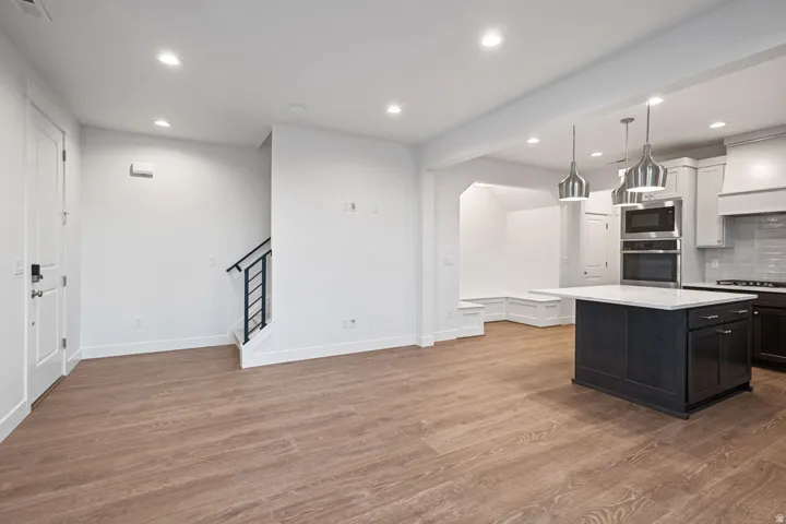 Dual tone kitchen featuring backsplash, stainless steel appliances, dark wood finished floors, light stone counters, and decorative light fixtures