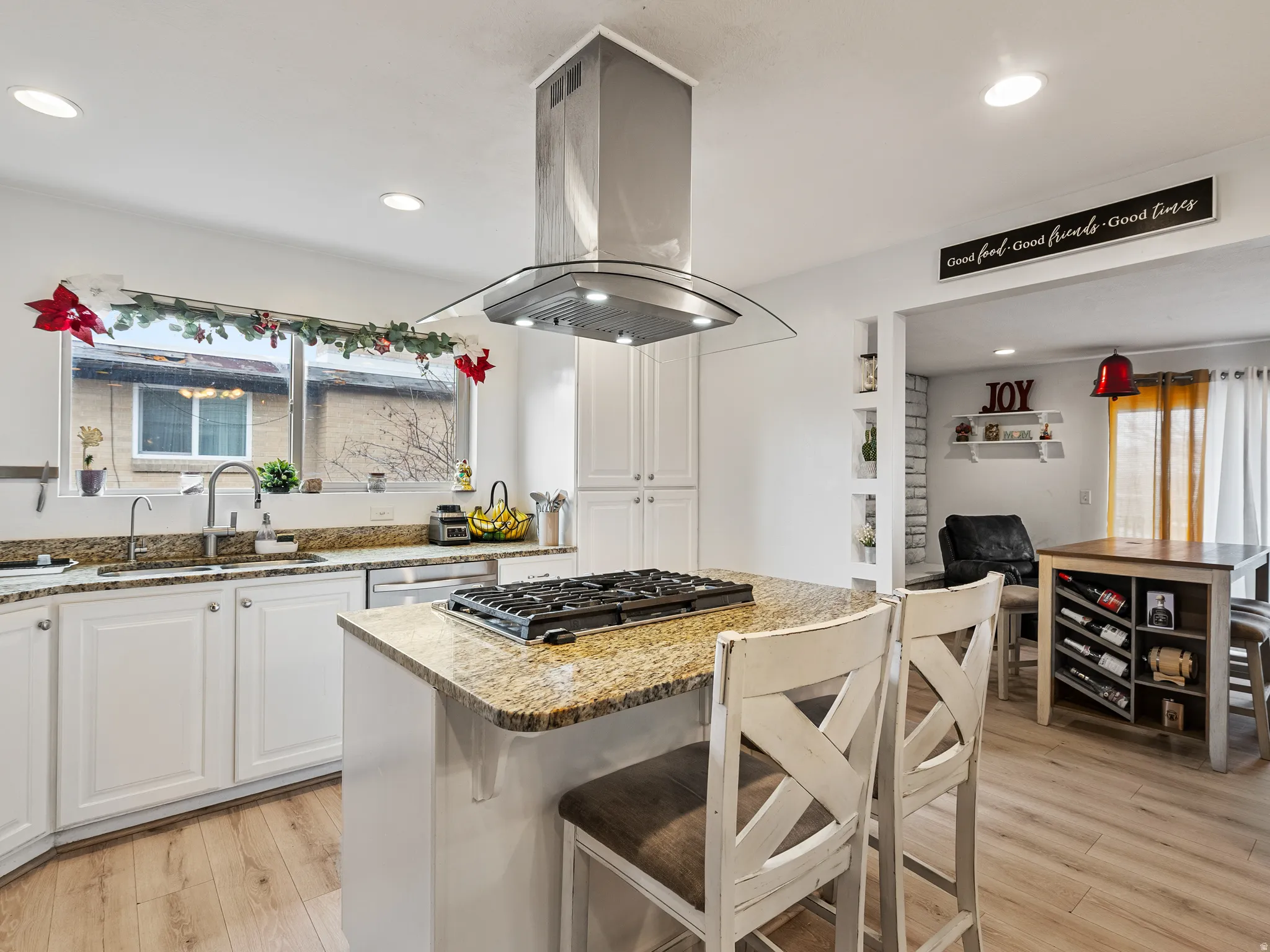 Kitchen with white cabinetry, a breakfast bar area, island exhaust hood, light stone countertops, and recessed lighting