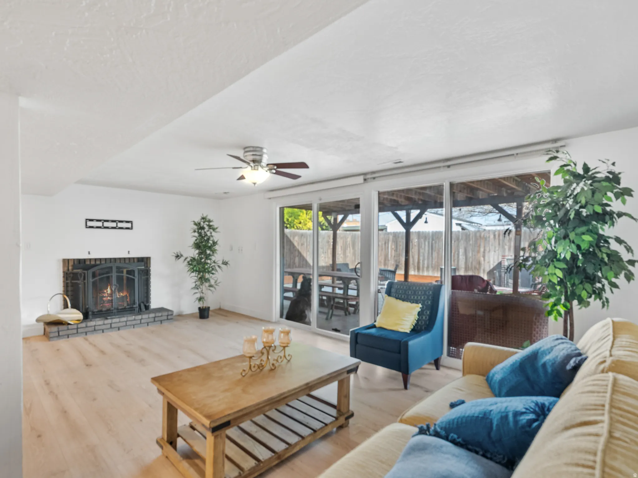 Living room featuring ceiling fan, wood finished floors, a brick fireplace, and a textured ceiling