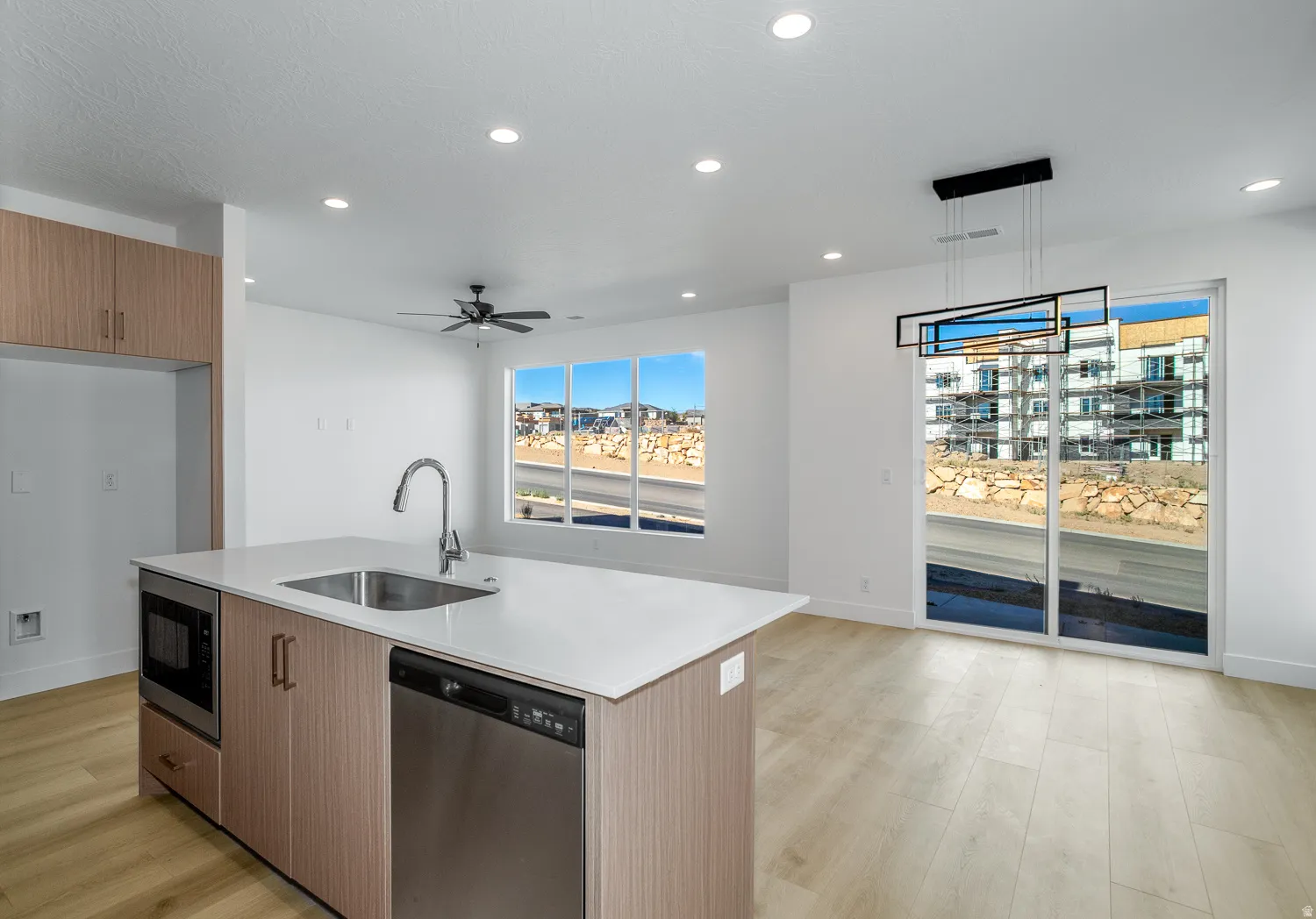 Kitchen with stainless steel appliances, a center island with sink, light stone countertops, modern cabinets, and light wood-style floors