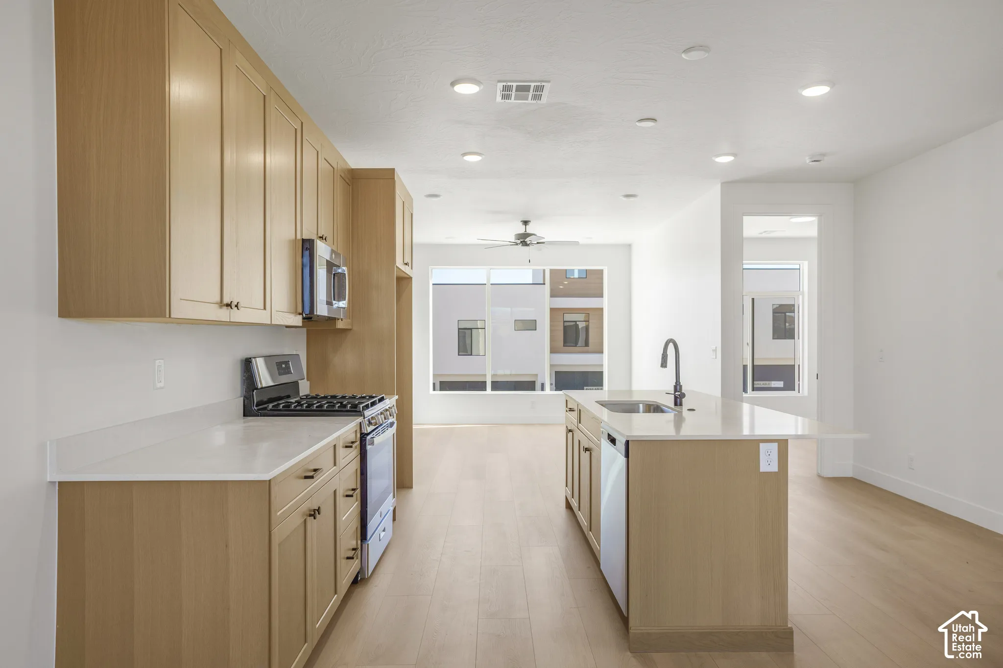 Kitchen featuring light-finish cabinetry, quartz countertops, a central island with an integrated stainless steel sink, wood-finish flooring, and recessed lighting