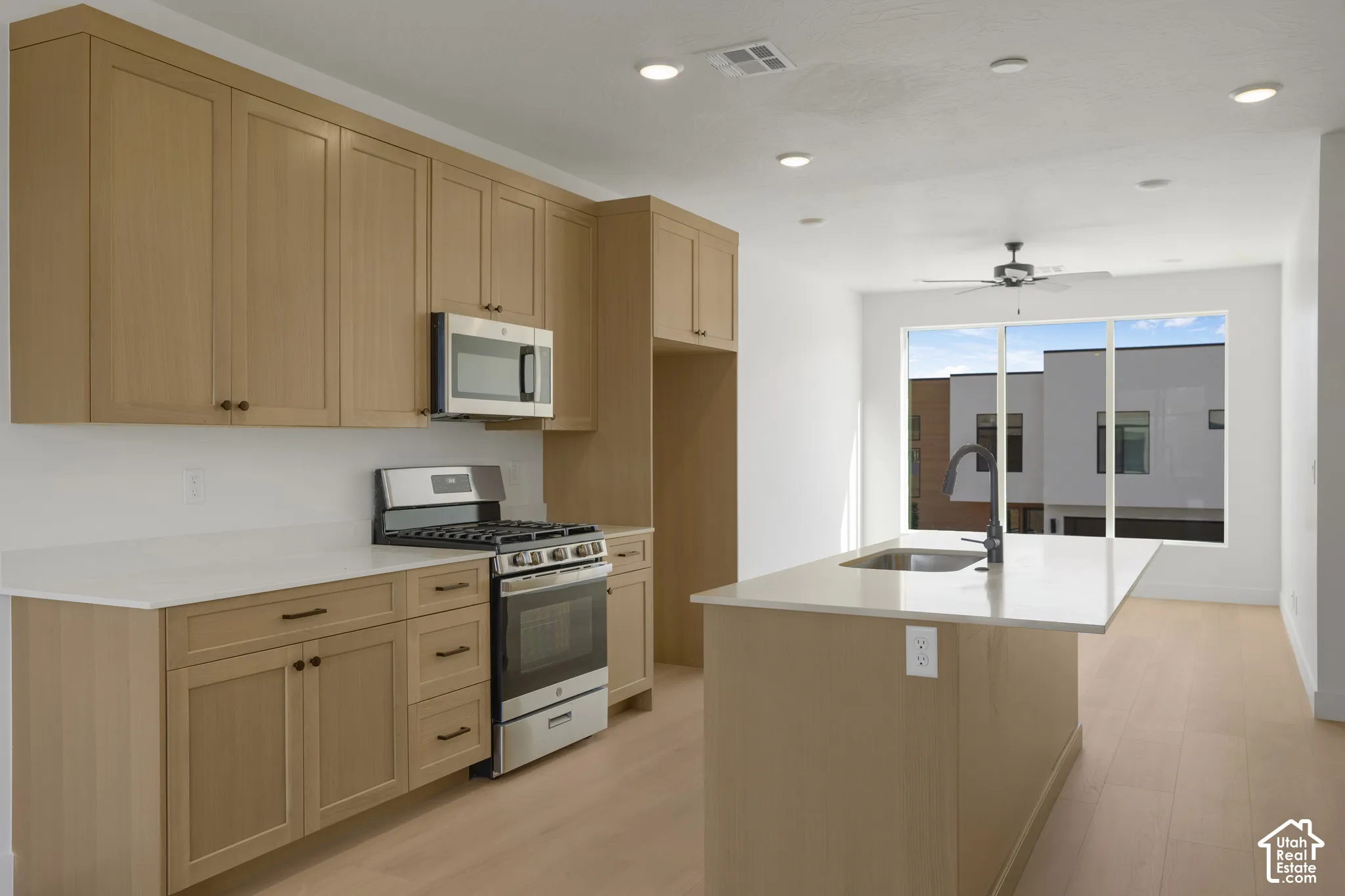 Kitchen featuring flat-panel wood cabinetry, quartz countertops, a central island with an undermount sink, stainless steel appliances, and wood-finish flooring