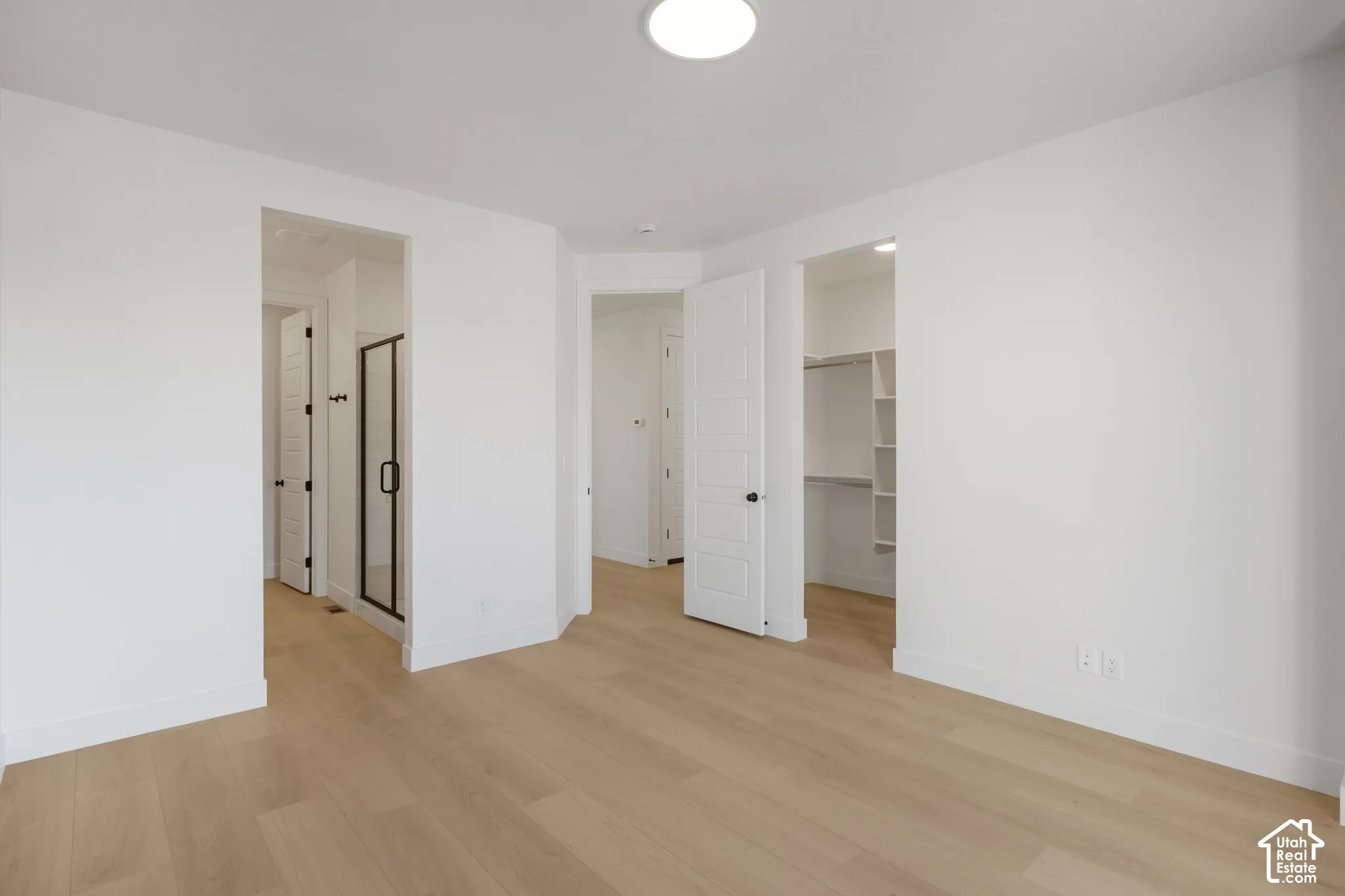 Neutral-toned wood-finish flooring, shaker-style interior doors, walk-in closet with built-in shelving, and a glass-enclosed shower featuring matte black hardware