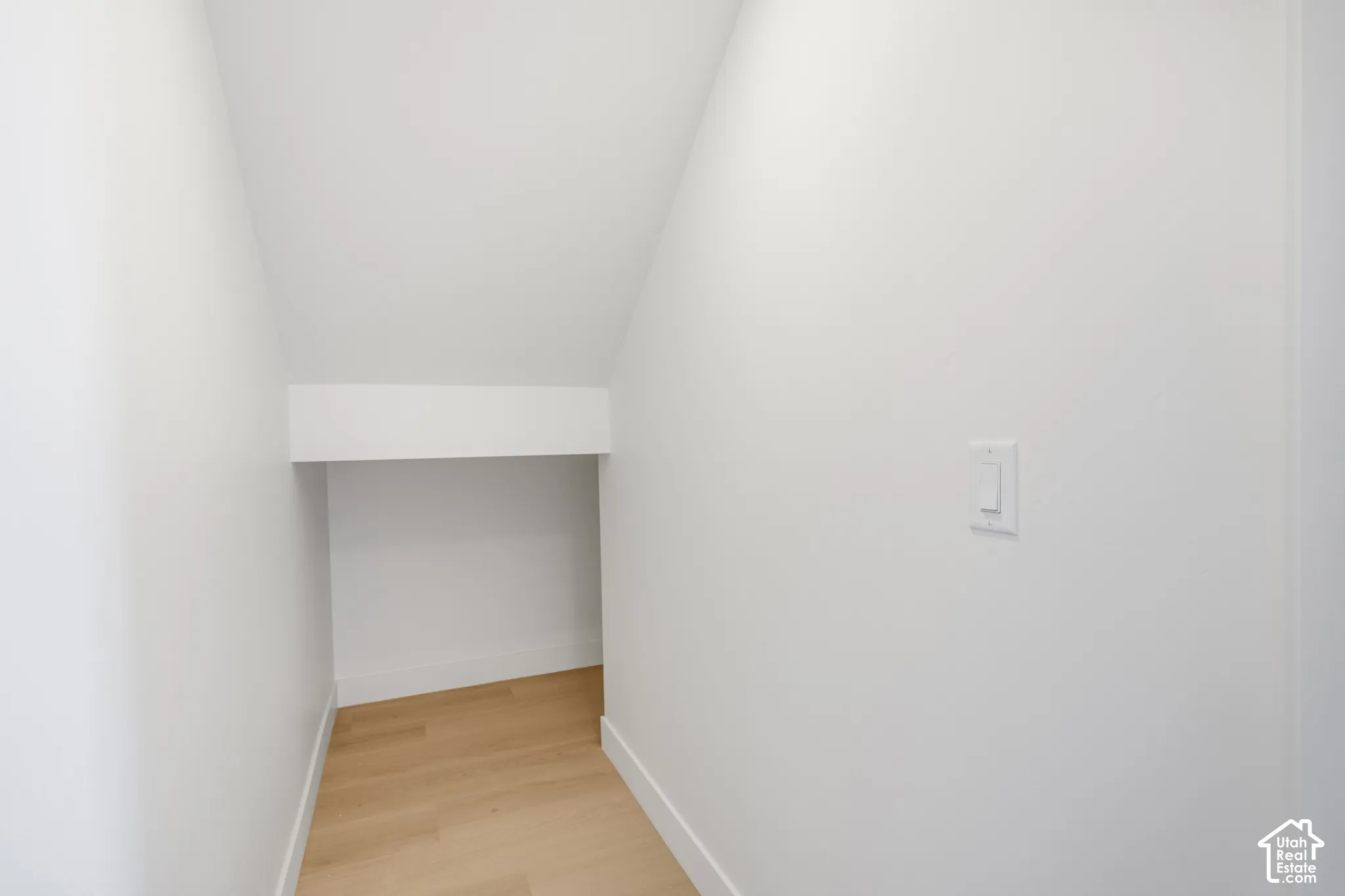 Storage alcove featuring neutral white walls and light-toned wood-finish flooring