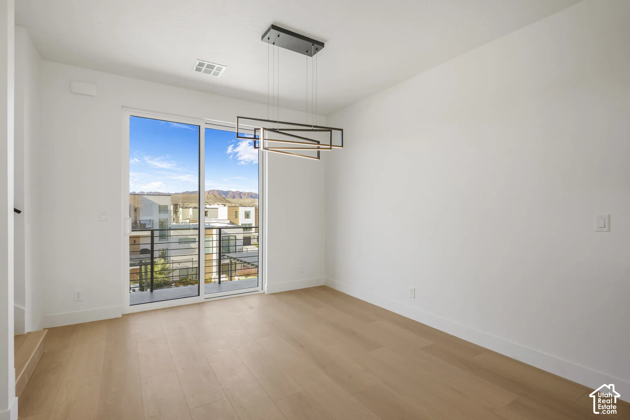 Modern space featuring wood-finish flooring, a geometric linear pendant light fixture, and sliding glass doors with access to a balcony