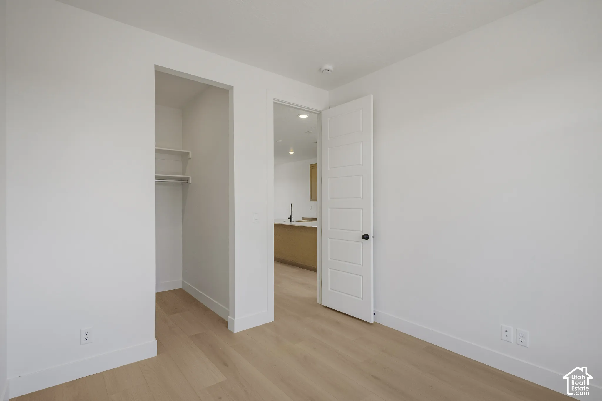 Room featuring wood-finish flooring, a five-panel interior door with matte black hardware, and an integrated closet with built-in shelving