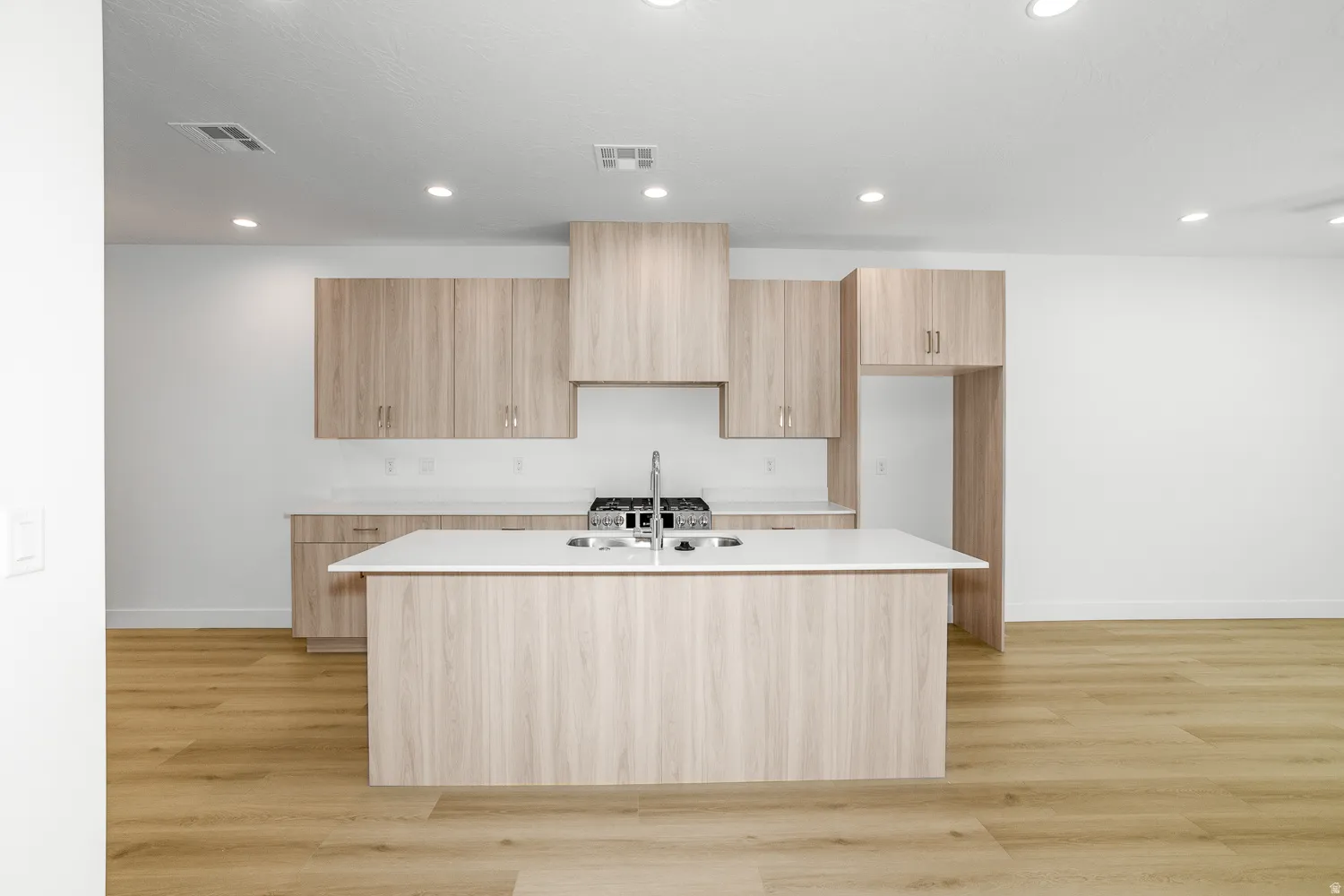 Kitchen featuring light wood-style floors, modern cabinets, a center island with sink, light wood finish cabinetry, and recessed lighting