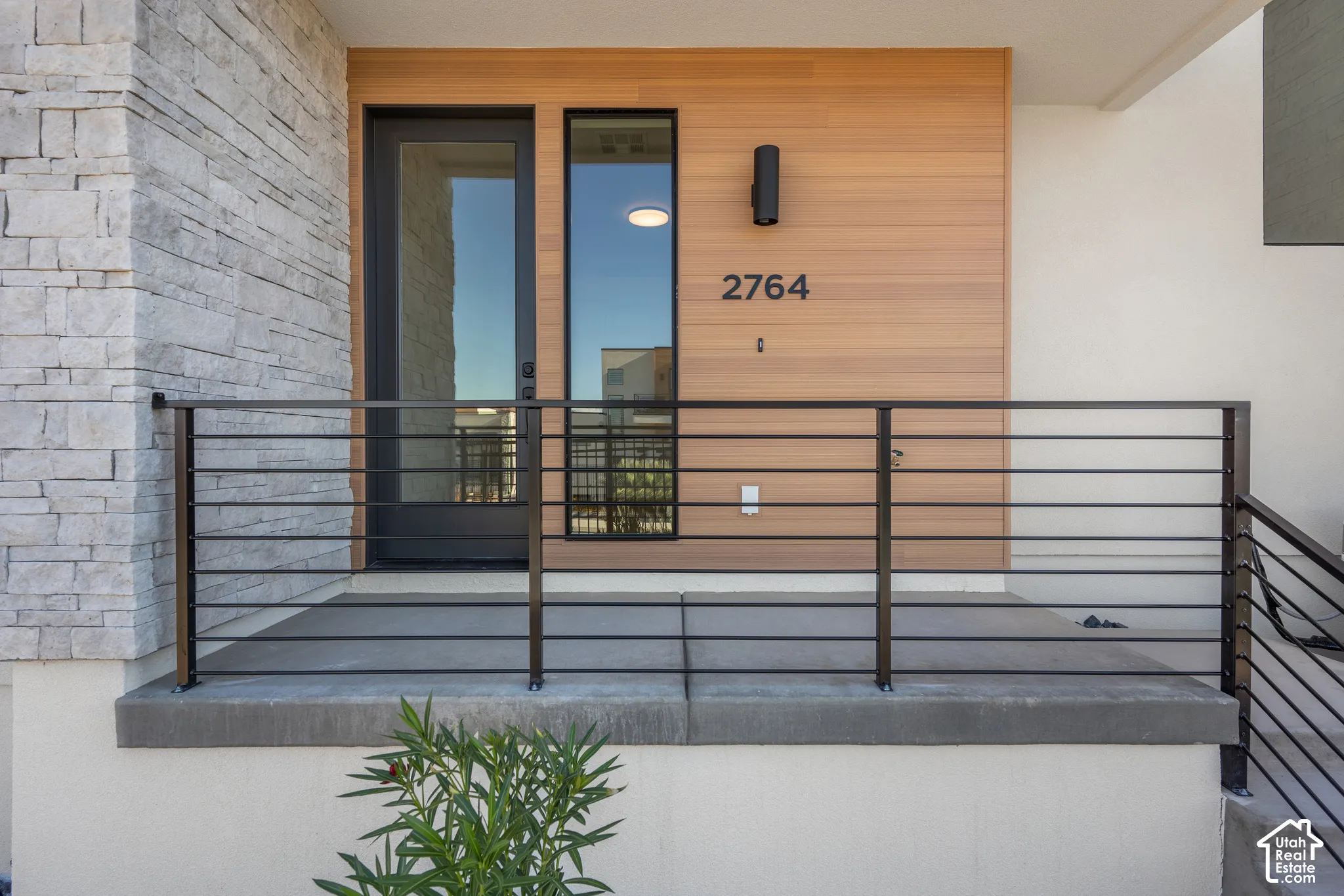 Exterior entrance featuring stacked stone masonry, horizontal wood-finish cladding, a glass-panel entry door, and a modern metal railing