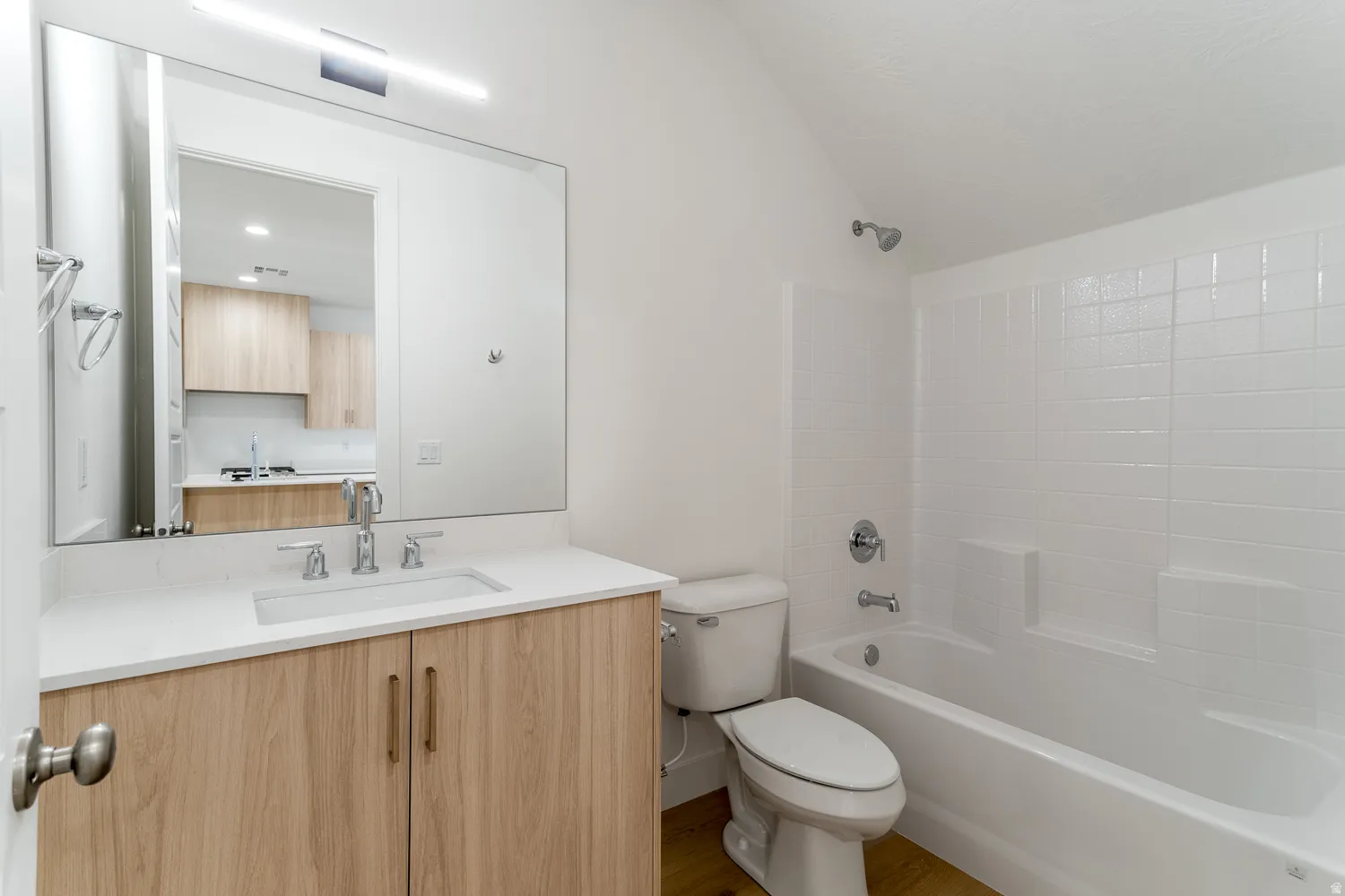 Bathroom with vanity, bathing tub / shower combination, dark wood-type flooring, and vaulted ceiling
