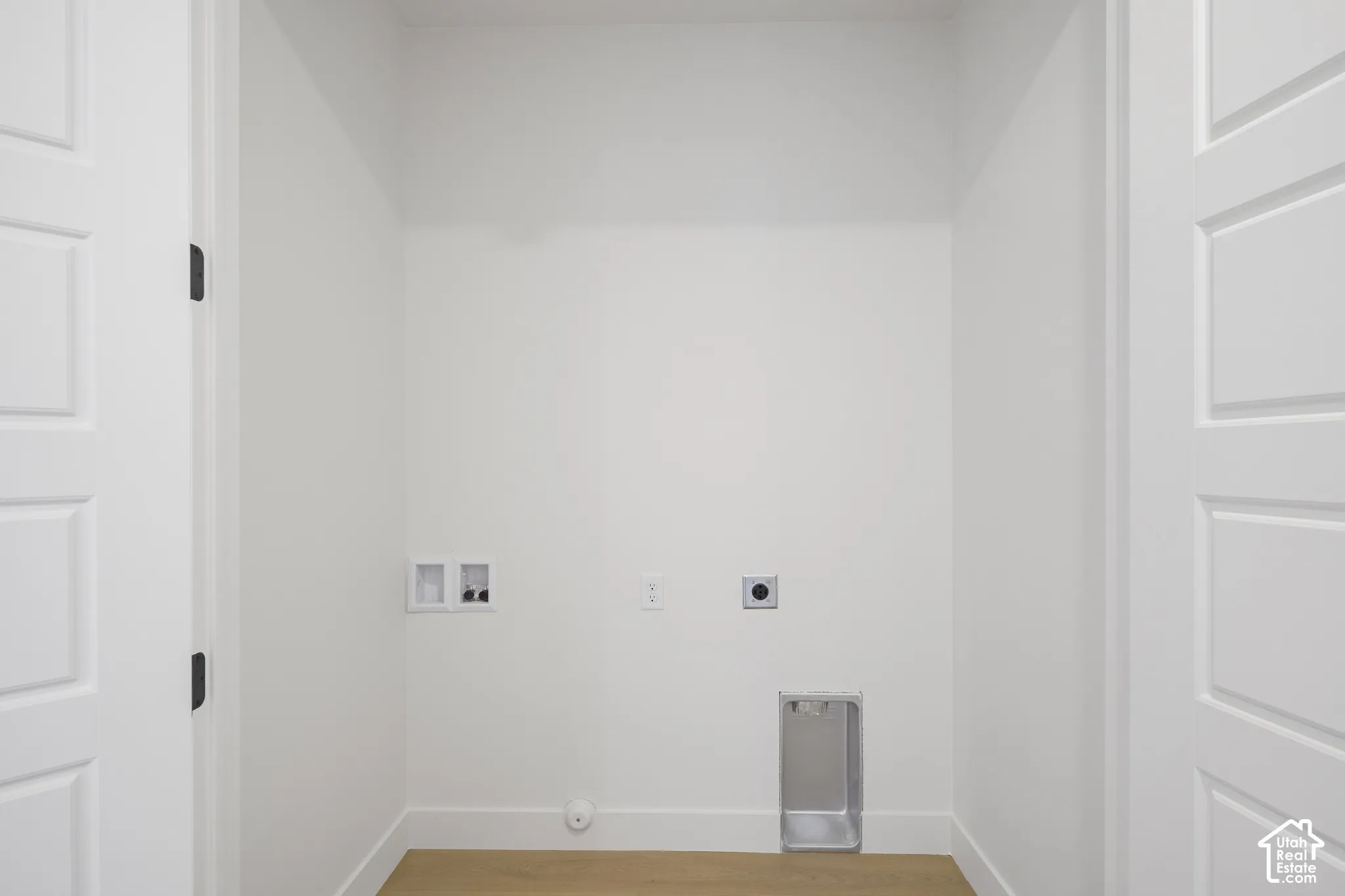 Dedicated utility area featuring white walls, wood-finish flooring, two multi-panel doors, and integrated electrical and plumbing hookups