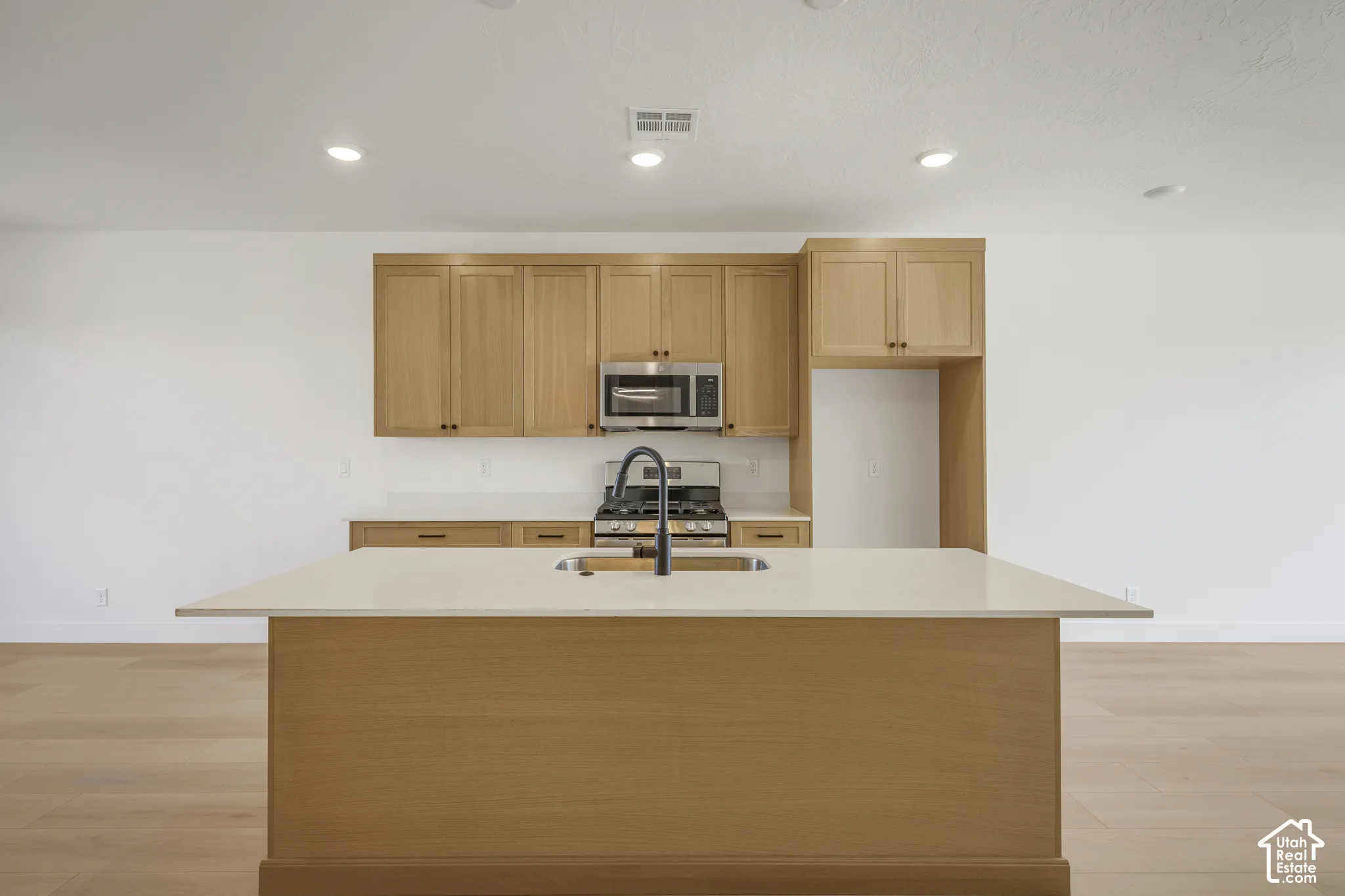 Kitchen featuring wood cabinetry, a central island with a solid-surface countertop, stainless steel appliances, a high-arc faucet, and wood-finish flooring