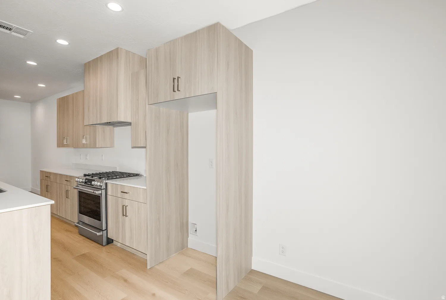 Kitchen with modern cabinets, stainless steel gas range, recessed lighting, light wood-style floors, and light stone countertops