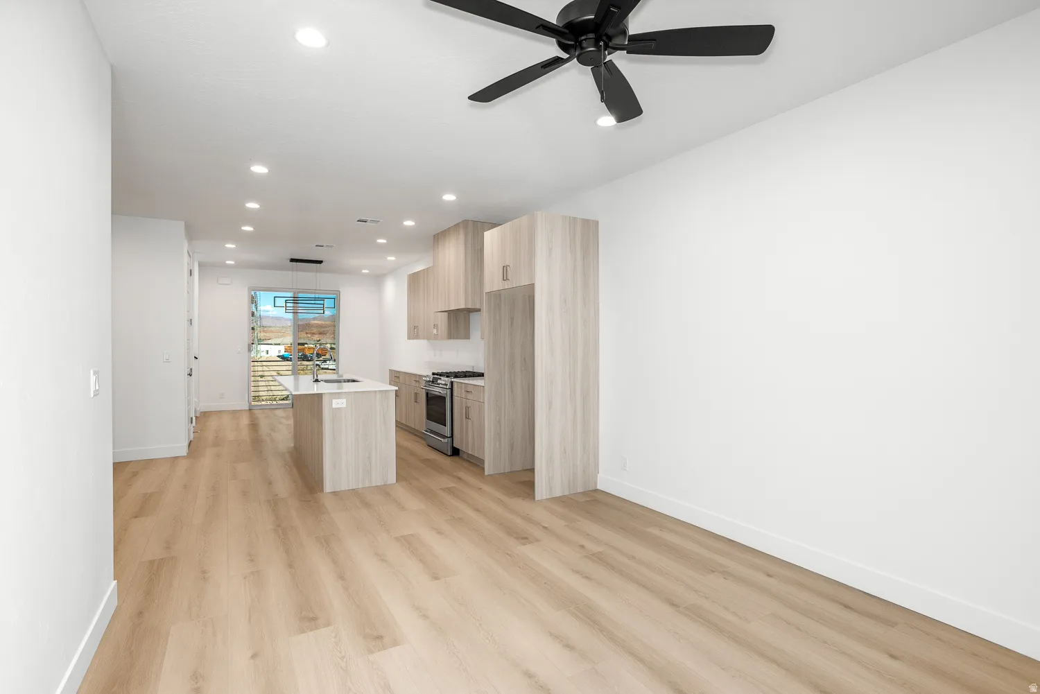 Kitchen featuring a center island with sink, modern cabinets, light wood finish cabinetry, a ceiling fan, and light wood finished floors
