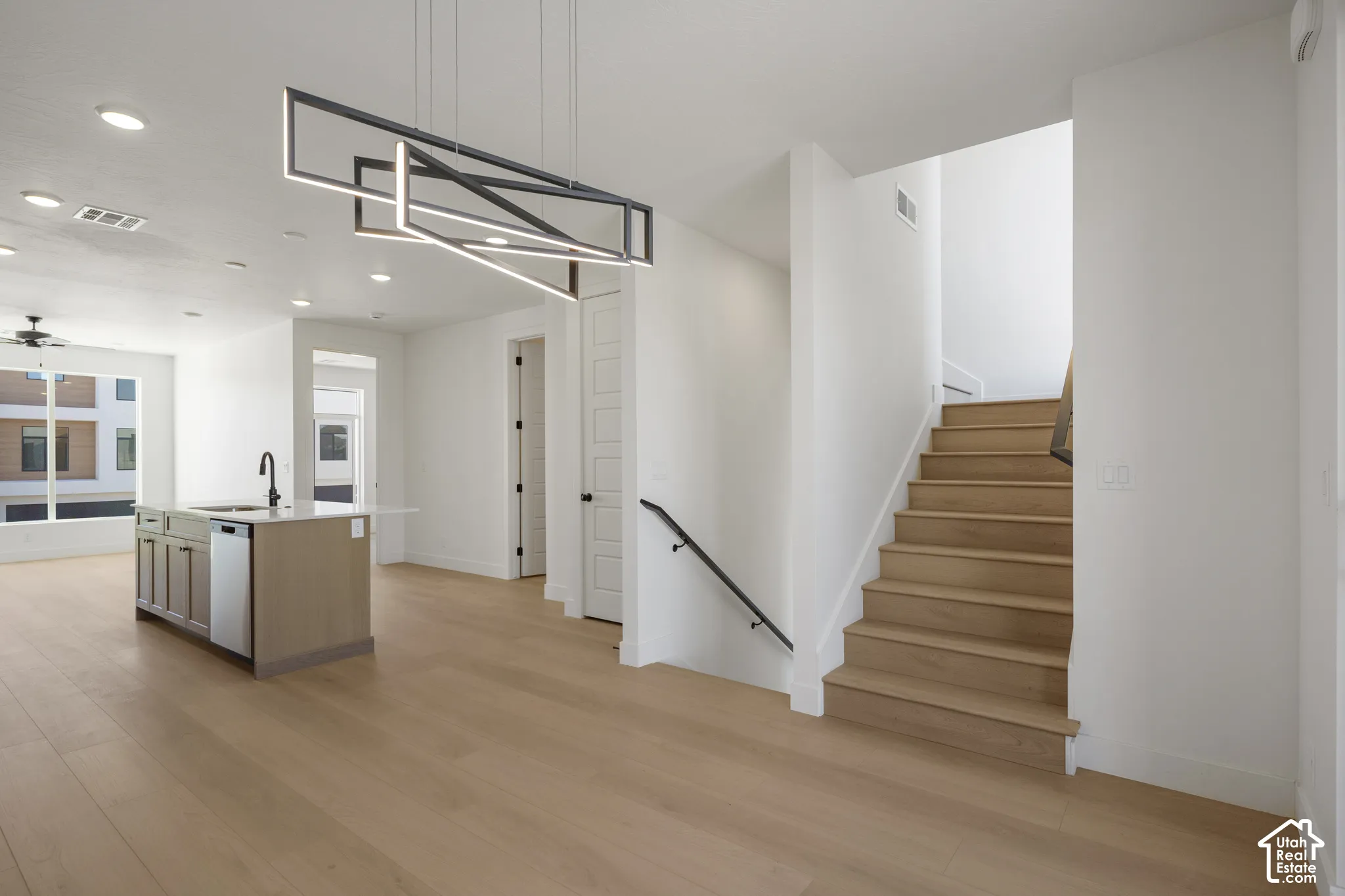 Modern kitchen island with quartz countertop and undermount sink, geometric LED chandelier, wood-finish flooring, and staircase with wood treads and matte black railing